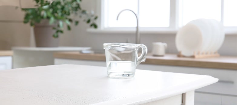Taza de vinagre blanco para trapear con una cocina impecable en el fondo