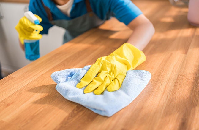 Persona con guantes amarillos desinfectando una superficie de madera con franela.