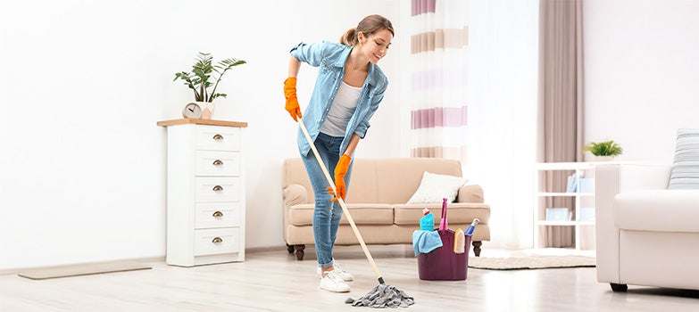 Mujer sonriente trapeando el piso de la sala de su casa, rodeada de un ambiente ordenado y acogedor. 