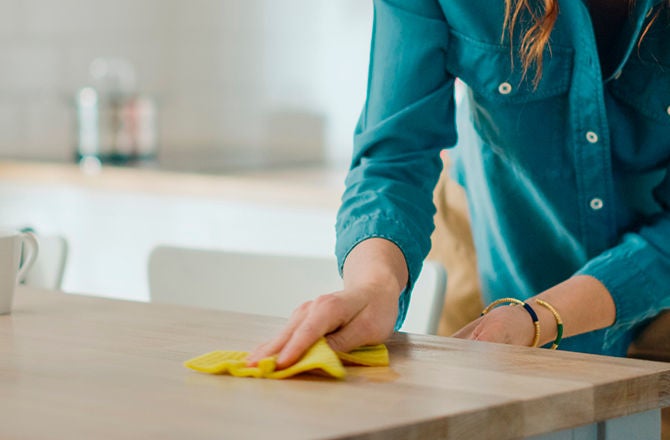 Persona limpiando y desinfectando una mesa de madera con un paño amarillo húmedo.