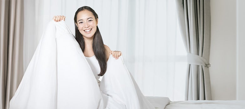 Mujer haciendo la  cama con sábanas blancas