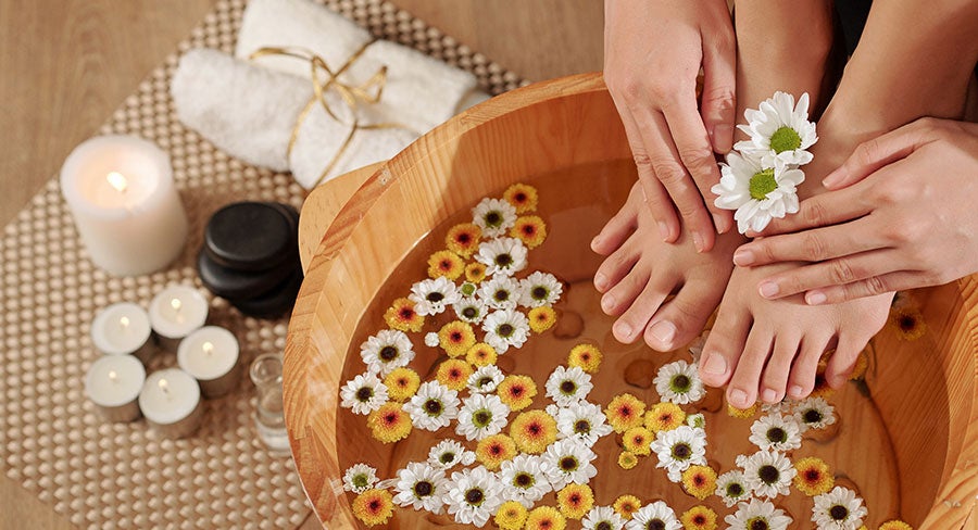 mujer colocando sus pies en una cuenca de madera con agua y flores