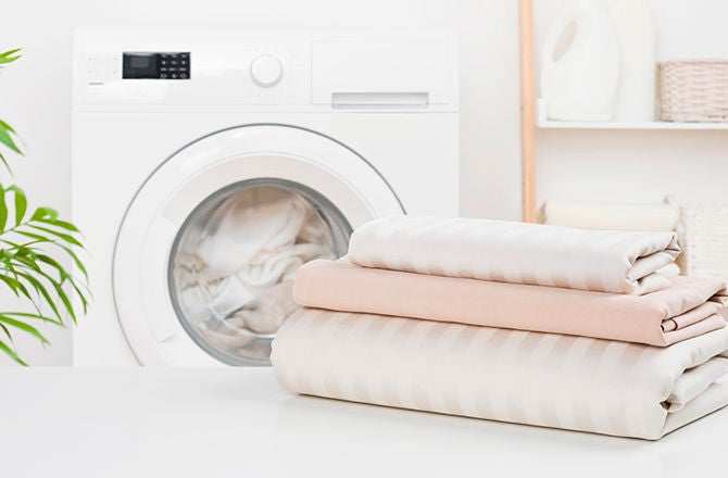 Sábanas limpias y perfectamente dobladas sobre una superficie frente a una lavadora moderna.